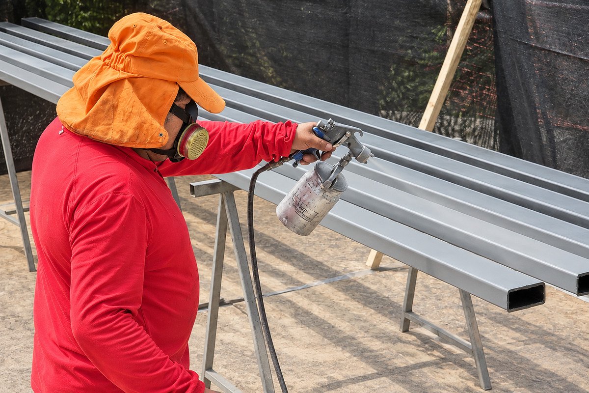 Maestro aplicando pintura a perfiles metálicos con pistola