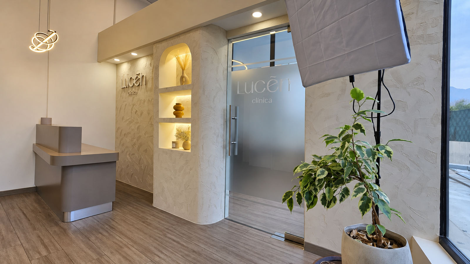 Recepción de Clínica Lucen con mesón, nichos iluminados y puerta de vidrio